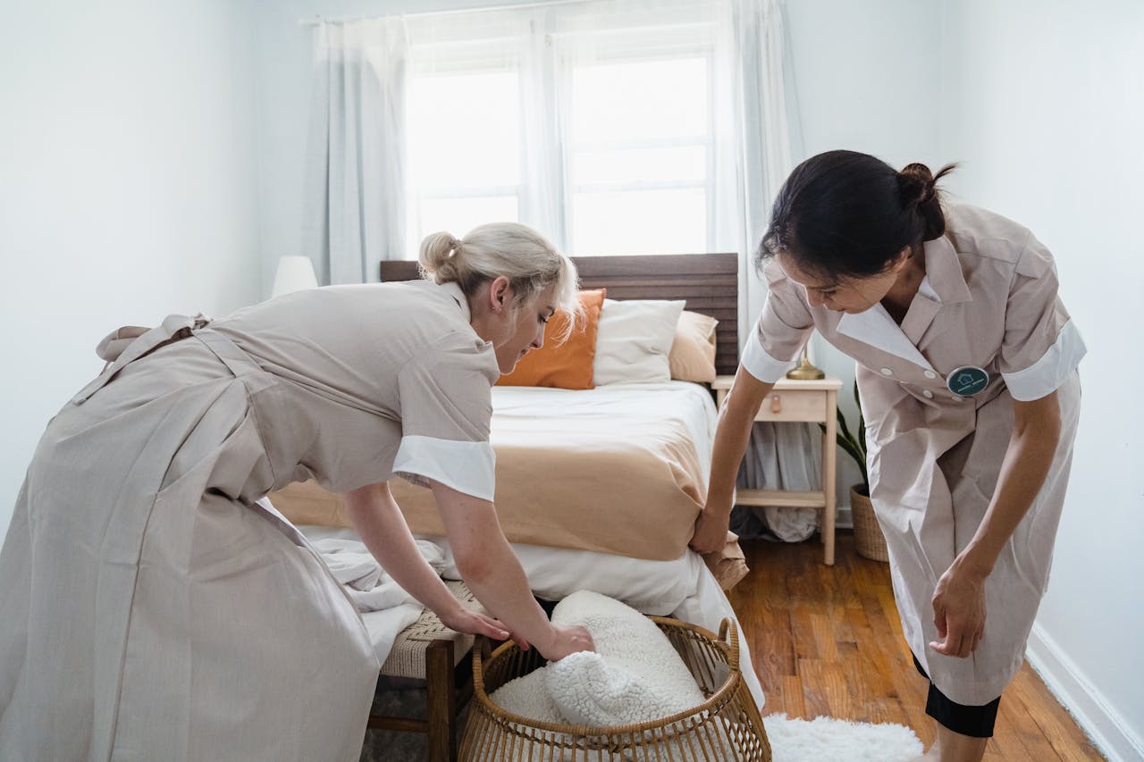 Two housekeepers organizing a bedroom, focusing on tidiness and comfort.